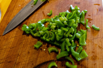 In the photo you can see the hands of a grandmother cutting small green peppers. the knife has a green handle. the pepper is cut into very small pieces to put them in the pan