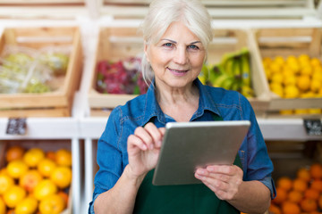 Shop assistant with digital tablet in small grocery store