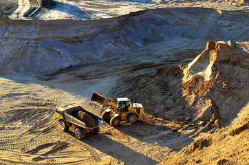 Wheel front-end loader unloading sand into heavy dump truck at the opencast mining quarry