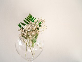 The border of delicate little white flowers on white background from front. Flat lay style. Space for text. Gypsophila on glass with leaf of fern