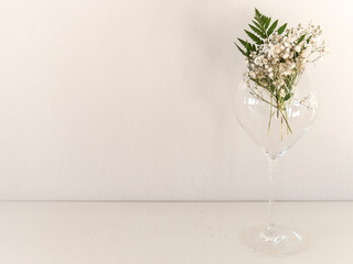 The border of delicate little white flowers on white background from front. Flat lay style. Space for text. Gypsophila on glass with leaf of fern