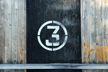 Number 3 in circle, on old rubber banner on stadium wall. White winner stamp with scratches on black background