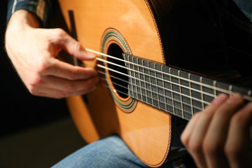 Fototapeta premium Man playing on classic guitar against dark background, closeup