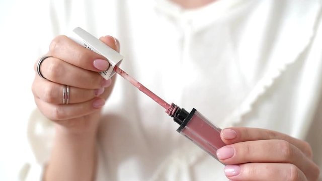 Manicured hands of a woman opening a tube of pink lip gloss, close up view on the applicator