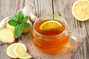 A glass cup of tea with lemon, mint and ginger on wooden rustic table.
