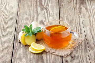 A glass cup of tea with lemon, mint and ginger on wooden rustic table.