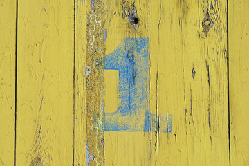 Number 1 on old wood dilapidated wall. Blue symbol with scratches on yellow background