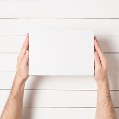 White rectangular box in male hands. Top view. White table on the background