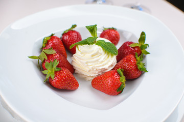 a ball of white ice cream with strawberries and mint on a white plate