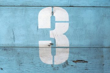 Number 3 on old wood dilapidated wall. White symbol with scratches on blue background