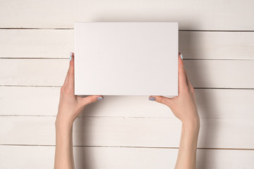 White rectangular box in female hands. Top view. White table on the background