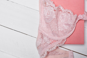 Pink lace bodice and notepad on white background. Fashionable concept. Close up