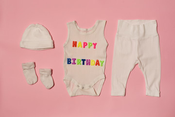 Set of clothes for the newborn. Colored inscription happy birthday on a pink background.