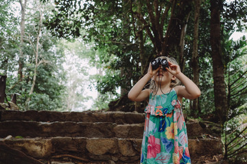 Little Funny girl looking through binoculars in the jungles on Seychelles