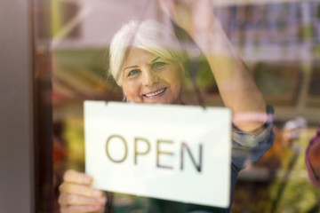 Senior woman holding open sign in organic produce shop