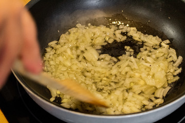 a grandmother stir in a pan of Asian type chopped onion with olive oil. stir the onion with a large wooden spoon which has a hole in the center