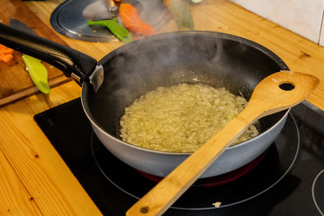a grandmother stir in a pan of Asian type chopped onion with olive oil. stir the onion with a large wooden spoon which has a hole in the center