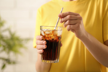 Woman holding glass of cola with ice on blurred background, closeup. Space for text