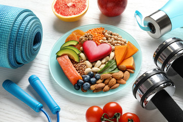 Plate with heart-healthy products and sports equipment on wooden background