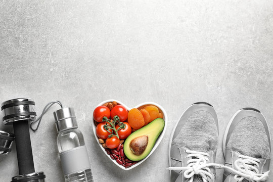 Heart-healthy products and sports equipment on grey background, flat lay. Space for text