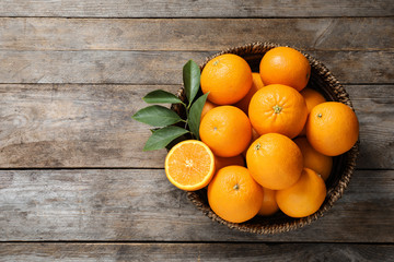 Wicker bowl with ripe oranges on wooden background, top view. Space for text