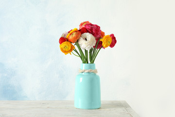 Vase with beautiful ranunculus flowers on table against color background