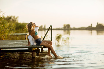 Young woman sitting on the pier on the lake