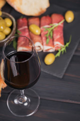 Glass of red wine with slices of cured ham or Spanish jamon serrano or Italian prosciutto crudo, bread, green olives and arugula