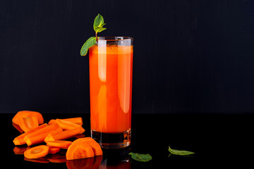 Glass of carrot juice with a some pieces of carrot on a black background. Raw carrot drink