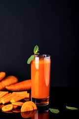 Glass of carrot juice with a some pieces of carrot on a black background. Raw carrot drink