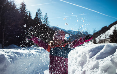 Kind wirft Schnee in Luft vor Winterkulisse
