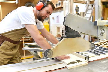 friendly carpenter with ear protectors and working clothes working on a saw in the workshop