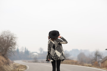 A woman in a beautiful gray cardigan and black hat rides along the way. Back view