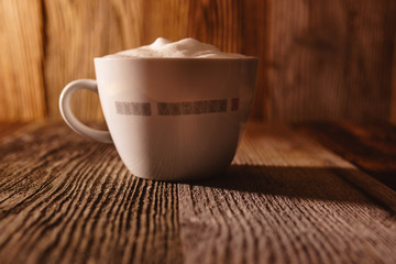 Cup of coffee with soy milk foam on wooden table in moody morning light