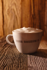 Cup of coffee with soy milk foam on wooden table in morning light - vertical
