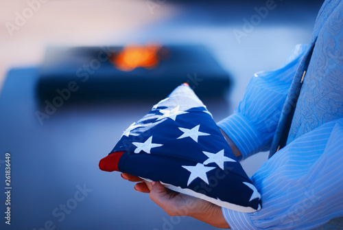 Happy Memorial Day. A girl holds a folded American flag in her hands, amid a blazing fire of memory. Concept for holidays of the United States of America.