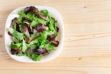 Template for a banner with a plate of green salad on a wooden background. Healthy food, vegetarians, diet. Basis for a banner with a plate of green salad. View from above