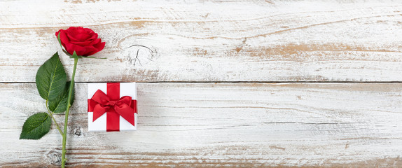 Anniversary background with a single red rose and gift box on white weathered wood