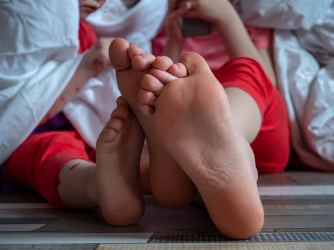 Caucasian children in pink t-shirt with smartphone on floor. Boys posing for camera under white blanket. One of children blond in glasses has chicken pox. Mom smeared follicles with pink solution