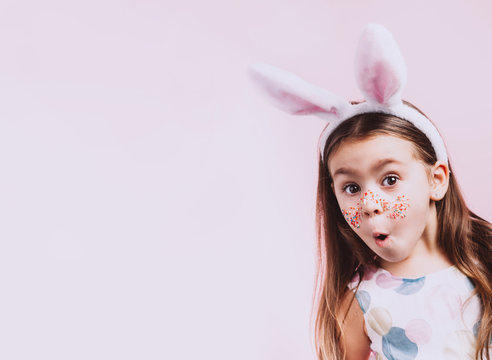 Naklejki Cute little girl with bunny ears on pink background. Easter child portrait, funny emotions, surprise. Copyspace for text.