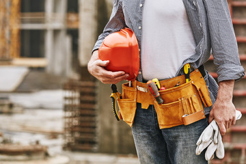 Construction safety. Cropped image of male builder with helmet and tool belt working at construction site - obrazy, fototapety, plakaty