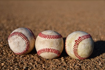 Photo of three game used baseballs on a baseball infield on a sunny day
