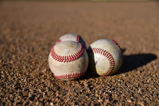 Photo of three game used baseballs on a baseball infield on a sunny day