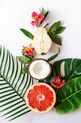 Summer tropical theme background or template with a space for a text, various fruits, green leaves and flowers. Bright summer background