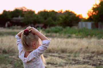 A young girl in a light clothing stands on a background sky in the evening at sunset somewhere in the Ukrainian village, selective focus.
