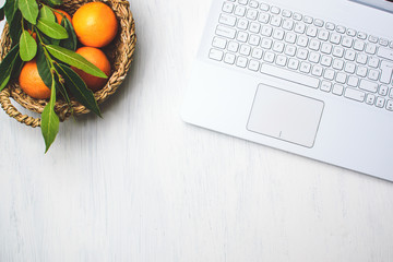 Flat lay top view of desk or work place with laptop and basket of fresh oranges