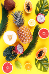 Exotic fruits and tropical palm leaves on pastel yellow background - papaya, mango, pineapple, banana, carambola, dragon fruit