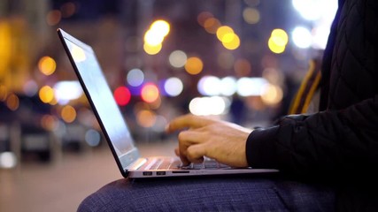 Close-up View of Man working at Laptop in the evening city street with bokeh light effect