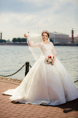 Fototapeta na wymiar Beautiful Bride in a white Wedding Dress outdoors with a Bouquet of flowers and a veil