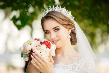 Beautiful Bride in a white Wedding Dress outdoors with a Bouquet of flowers and a veil